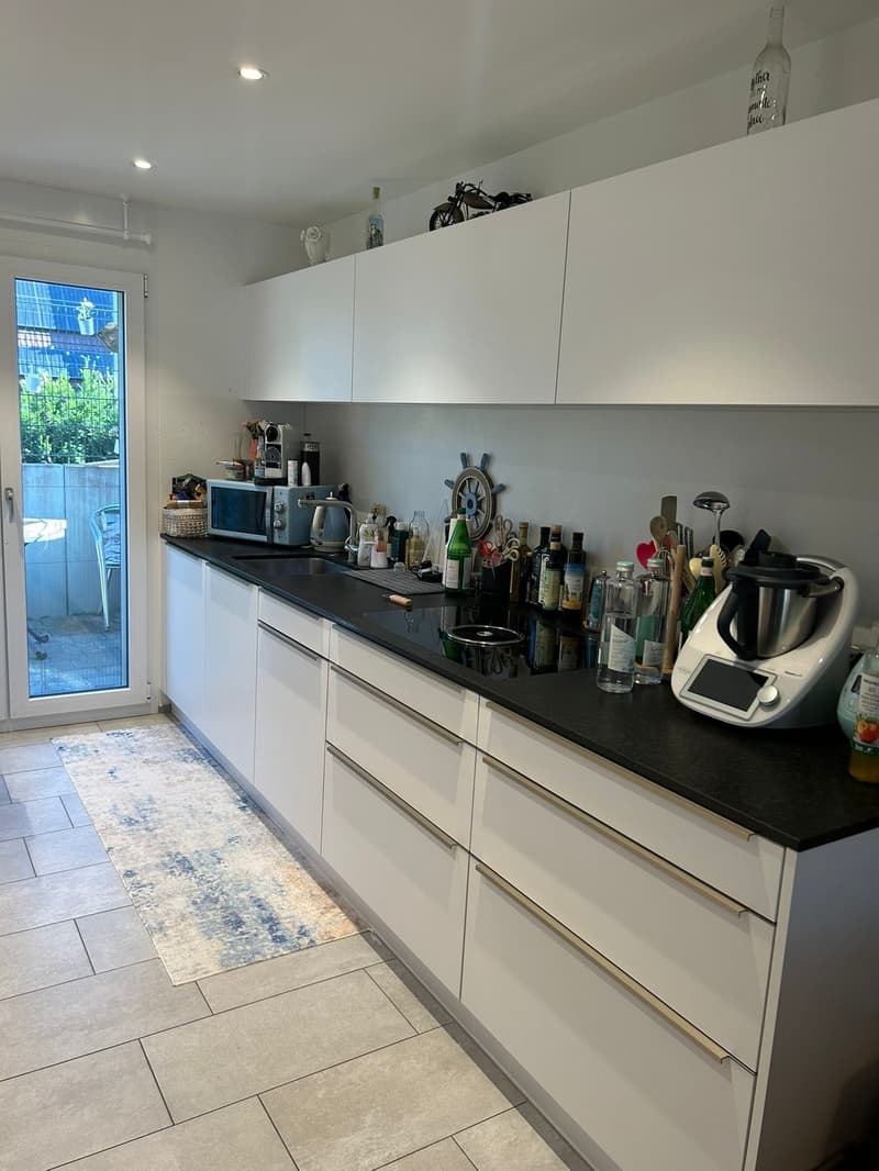 modern kitchen with white cabinets, black countertops, built-in appliances, and a glass door leading to a patio