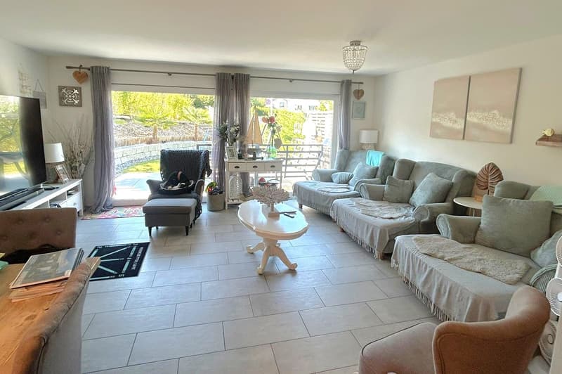 large living room, white walls, white tile floor, large windows, balcony, sofa, coffee table, armchairs, TV, side table, rug