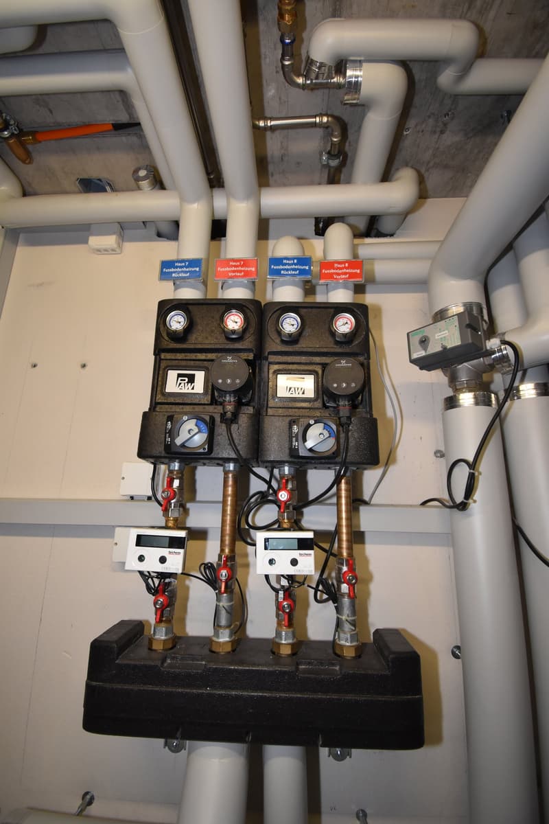 Two heating system units with gauges, pipes, and valves attached to a wall