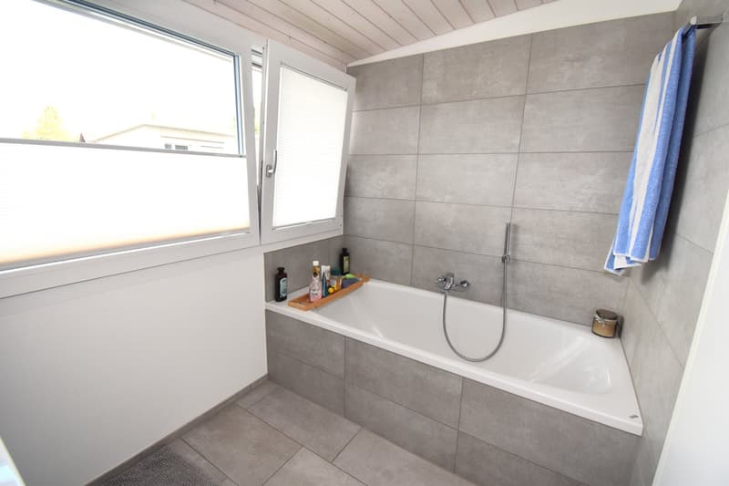 Bathroom with bathtub, window, tiled walls, and floor, towel rack, toiletries on tray
