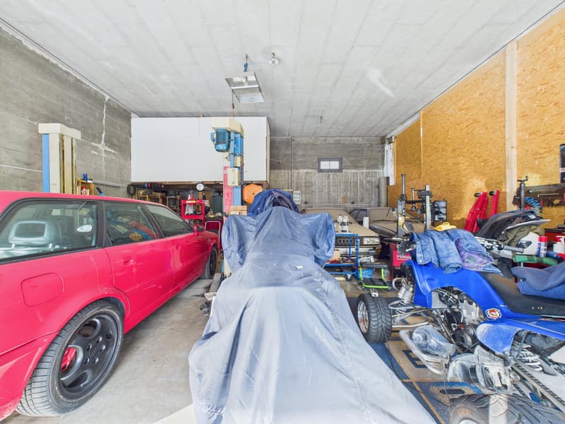 Red car, blue cover, motorcycle, various tools and machines, shelves with items, concrete walls, wooden walls, lamps
