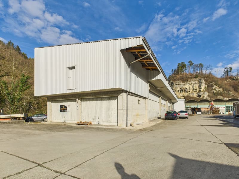 A white industrial building with a metal roof, two large garage doors, and several parked cars in front.