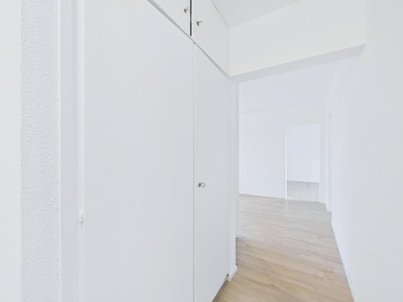 empty room with wooden floor and white walls, two white doors, one closed and one leading to another room