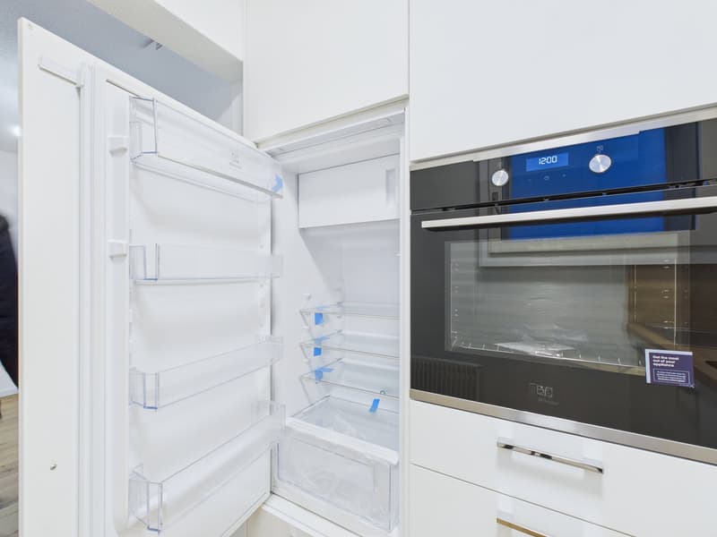 Modern kitchen with white cabinets, open refrigerator, and built-in oven