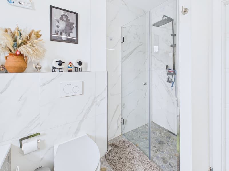 modern bathroom, white marble tiles, glass shower enclosure, white toilet, white sink, decorative items on the shelf