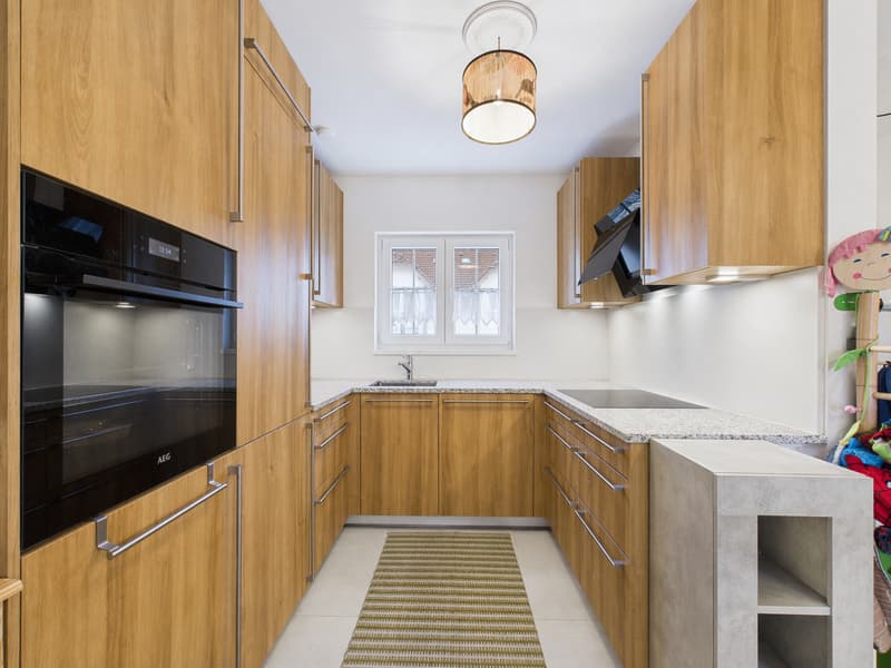 modern kitchen with wooden cabinets, granite countertops, AEG oven, sink, faucet, dishwasher, and a rug