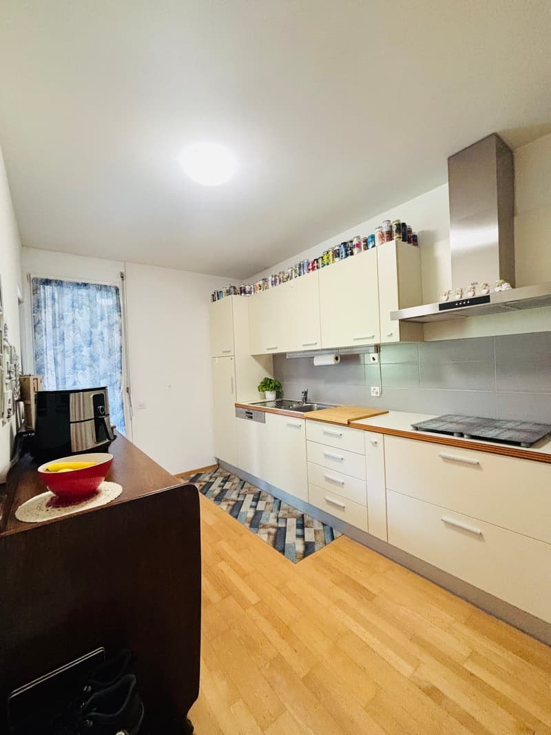 Spacious kitchen with white cabinets, wooden countertops, and a dishwasher. The floor is made of hardwood and there is a colorful mosaic tile backsplash. The kitchen also has a large window providing natural light.