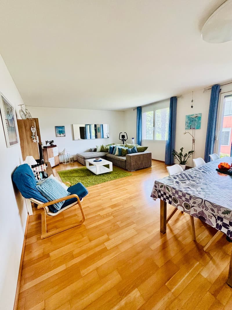 Open living room with hardwood floor, sofa, dining table, and wooden chair, white ceiling, white walls, coffee table, carpet, and picture frames