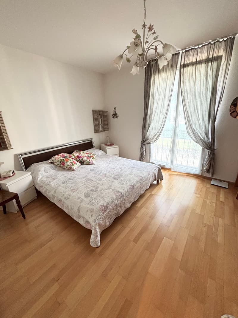 wooden floor, large bed, floral bedding, nightstands, chandelier, sliding glass door, balcony, curtains