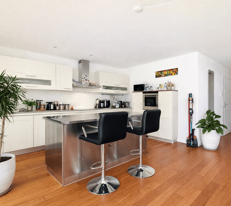modern kitchen with island, stainless steel bar stools, white cabinets, wooden floor, plants, appliances