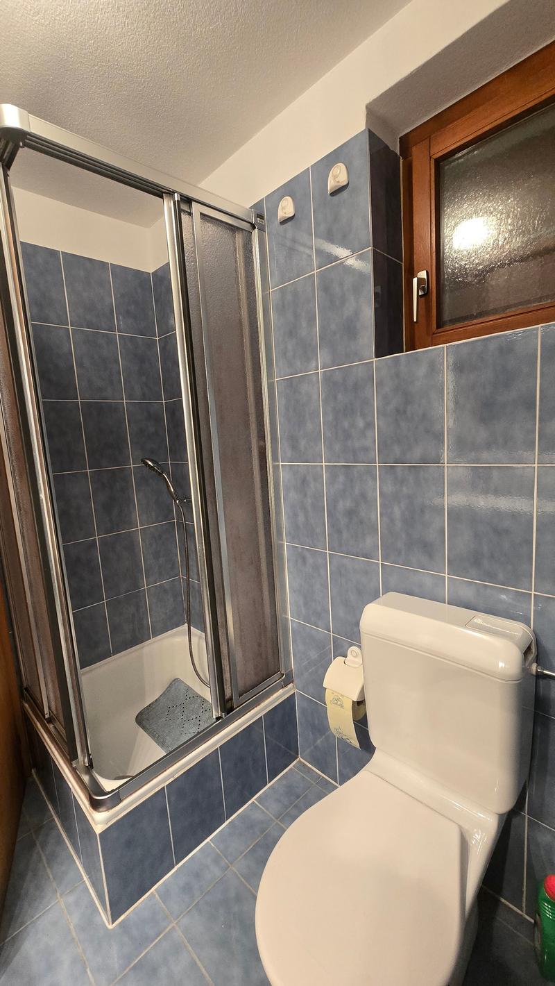 A modern bathroom with blue tiles, glass door shower, white toilet, and small foot mat.