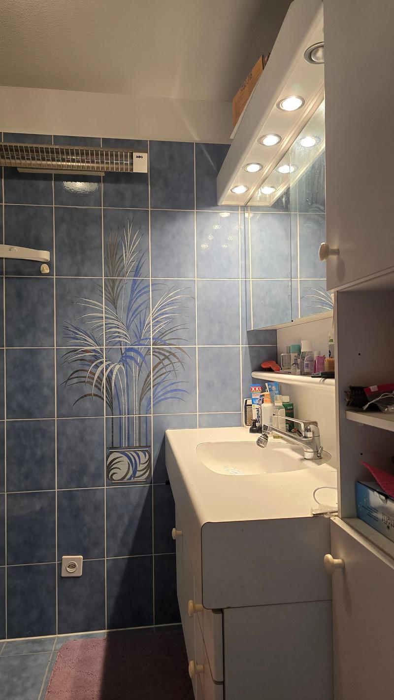 Bathroom with blue tiled walls, a white sink, blue tiles, an overhead mirror with lights, and a cabinet with shelves.