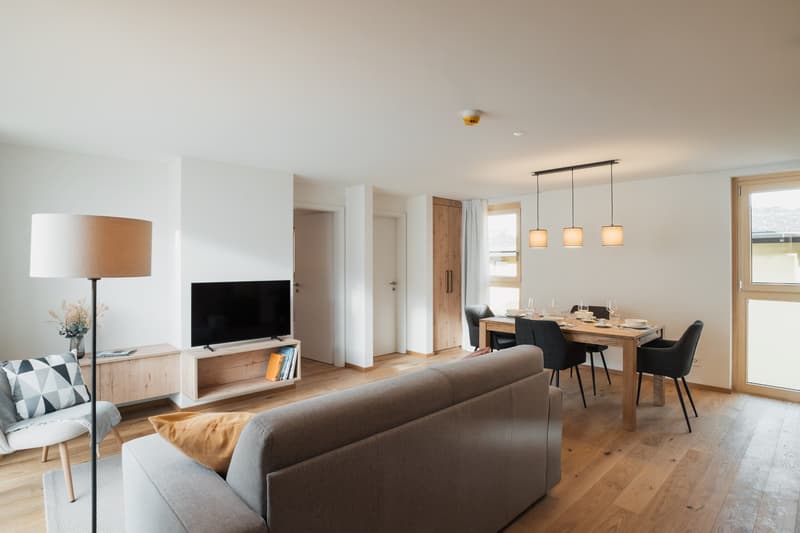 Modern living room with a view to the outside. It has wooden floors and a dining area with a wooden table and chairs.