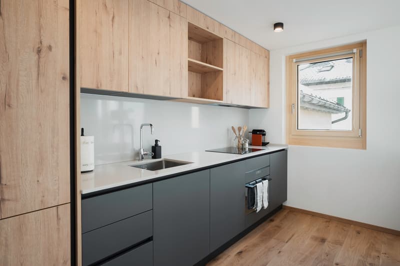 Modern kitchen with wooden cabinets, granite countertop, stainless steel sink, built-in dishwasher, electric stove, wooden floor.