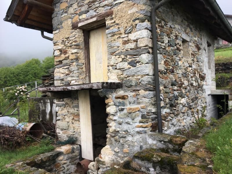 Old stone house, raised ground floor, wooden door, small window, open entrance, stone structure
