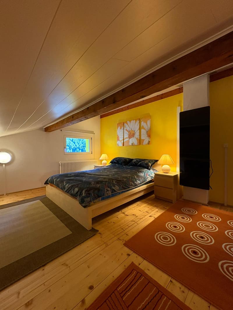 Bedroom with wooden bed, lamps, carpet, radiator, and paintings on the wall.