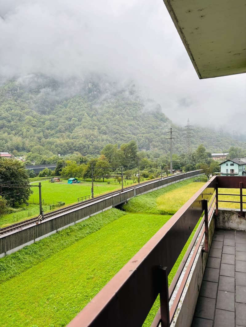 Railway tracks, grassy fields, mountainous terrain, wooden fencing, small structures in the distance