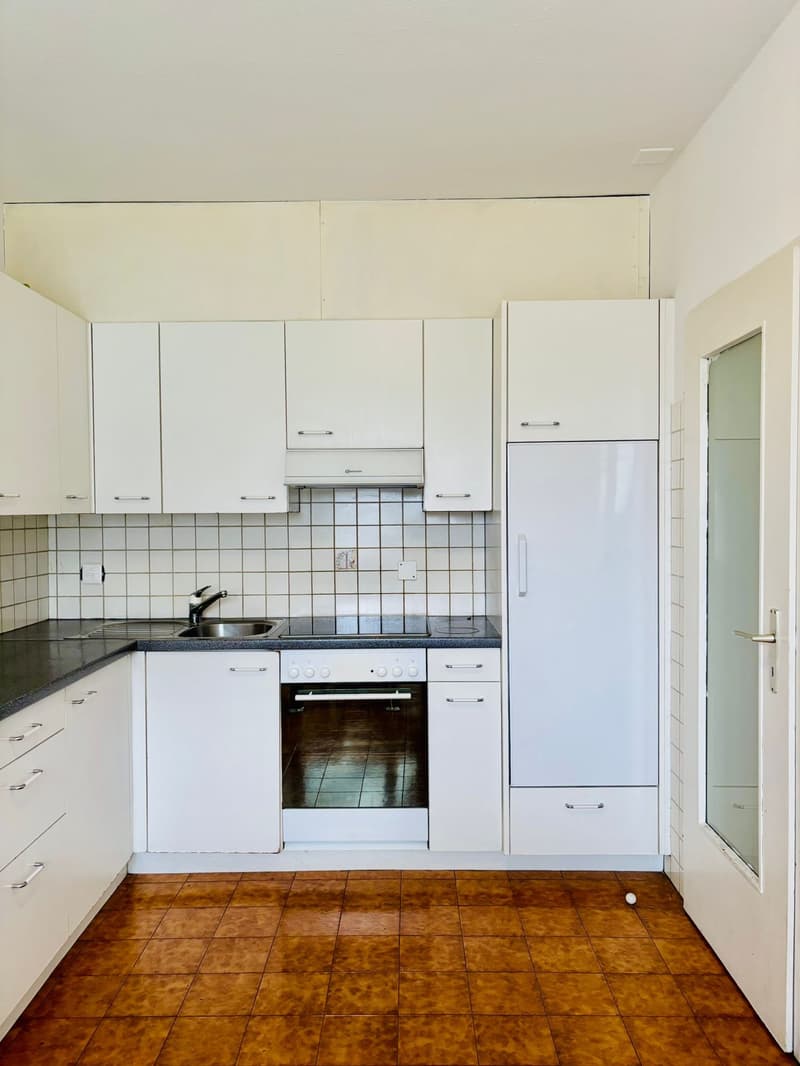 Modern kitchen with white cabinetry, tiled backsplash, stainless steel appliances, brown tile flooring, overhead cabinets, sink, and countertop