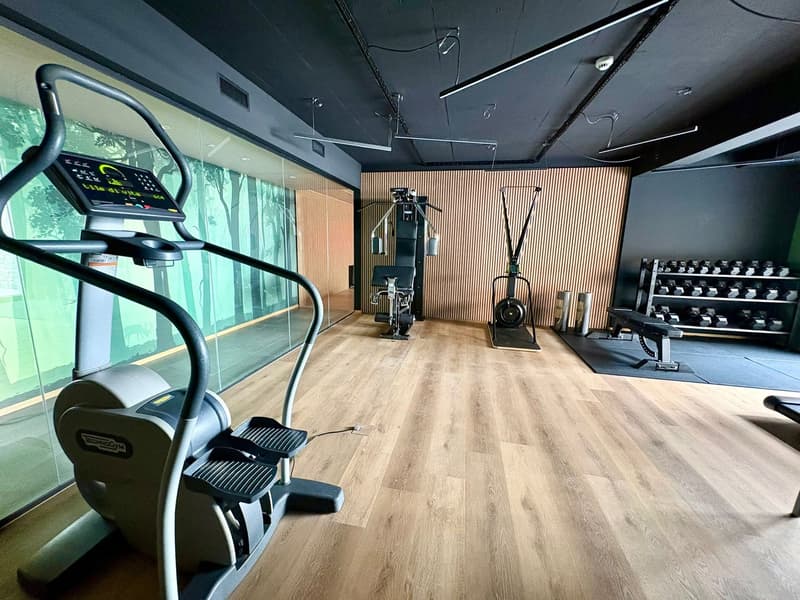 A gym room with various exercise equipment, wooden floors, and glass walls.
