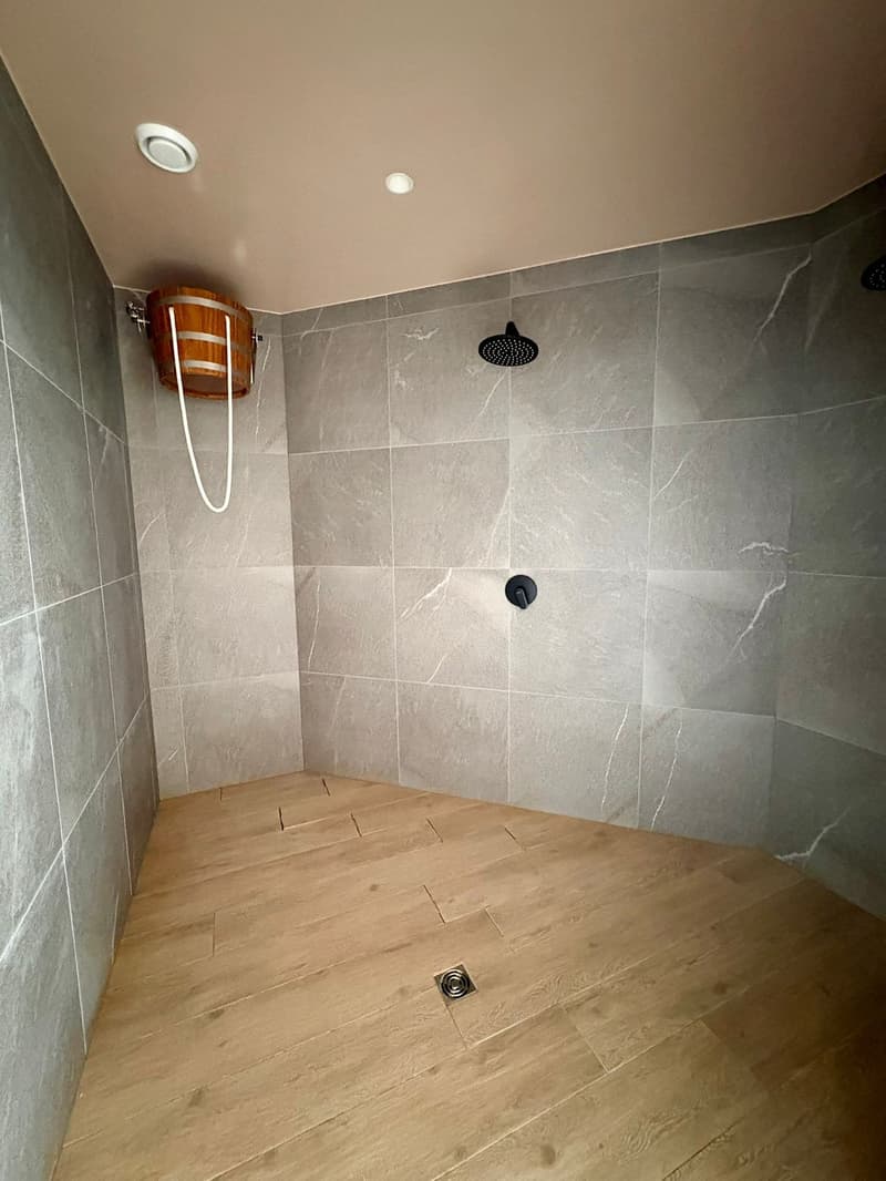 The shower area has a wooden barrel, floor drain, and a shower head.