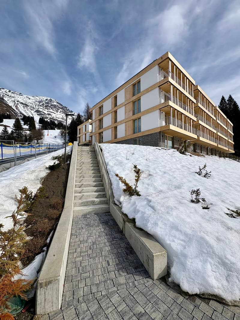 Modern wooden and stone building, multiple balconies, multiple levels, snow-covered hill