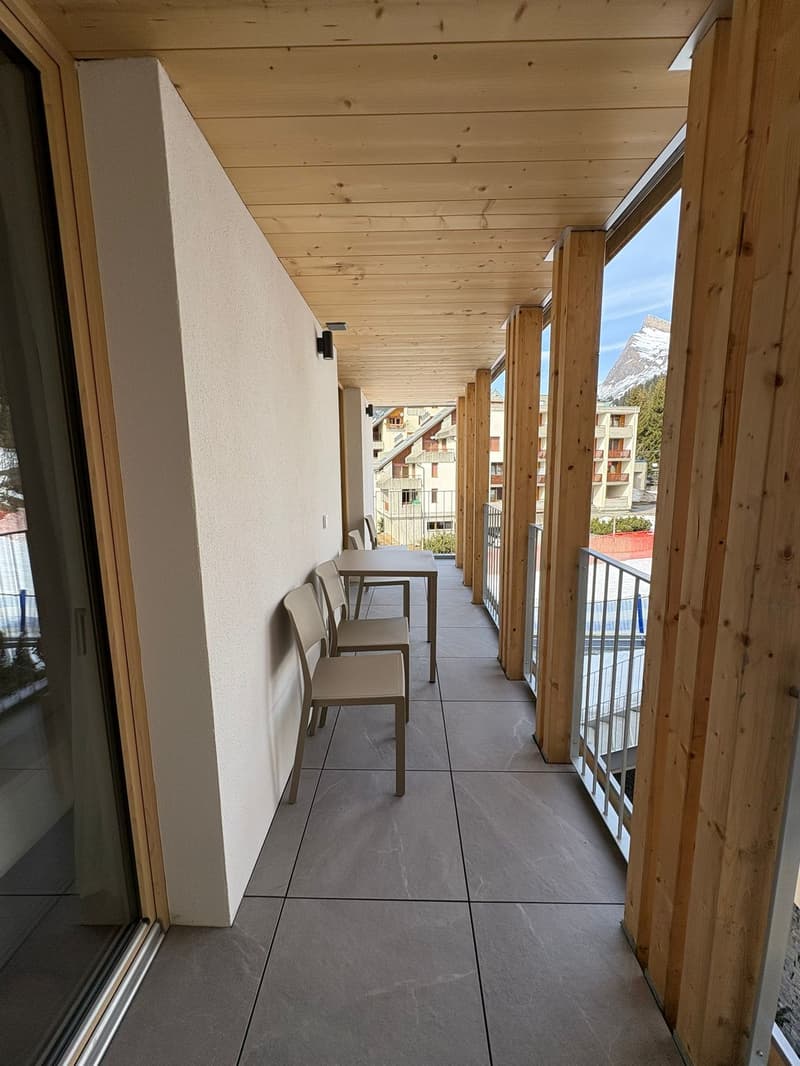 terraced area with wooden floor, large glass windows, outdoor table and chairs, railings, view of the mountains and surrounding area