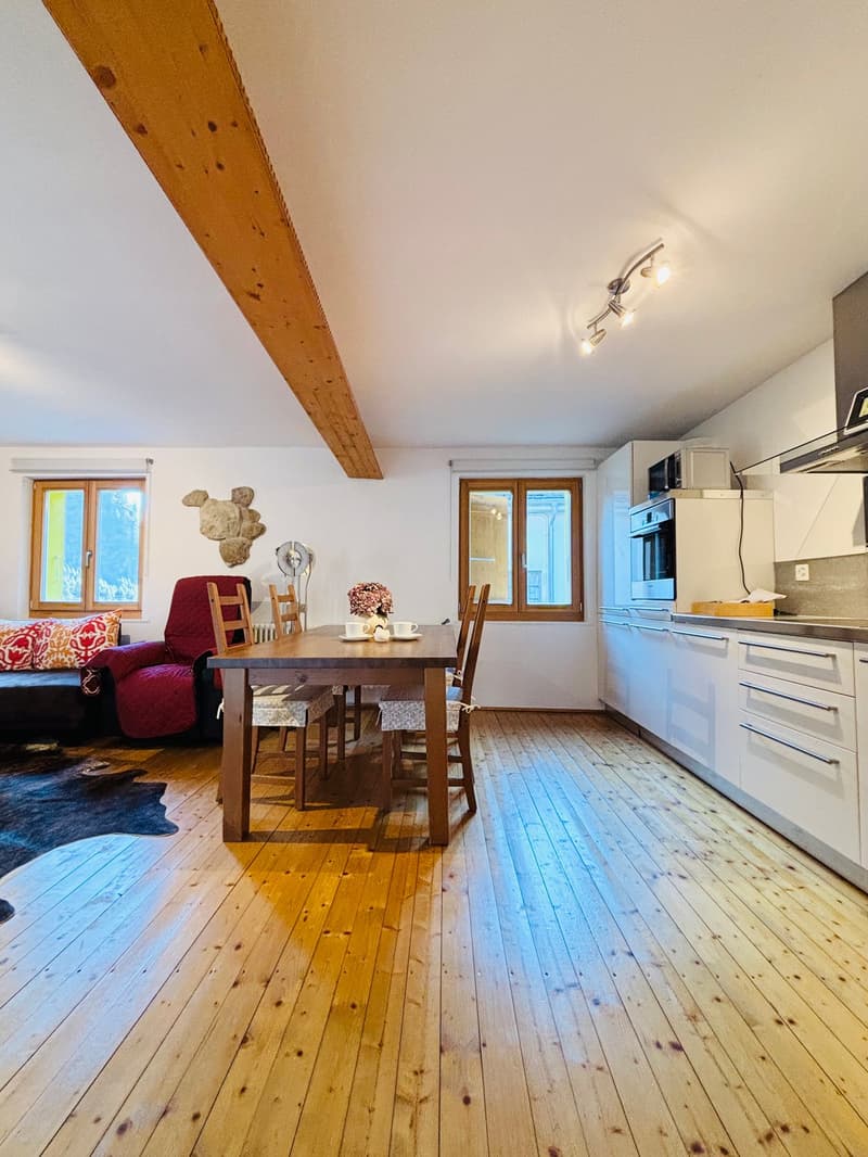 Dining room with wooden floor, wooden table, chairs, white kitchen, couch, windows, wooden beam