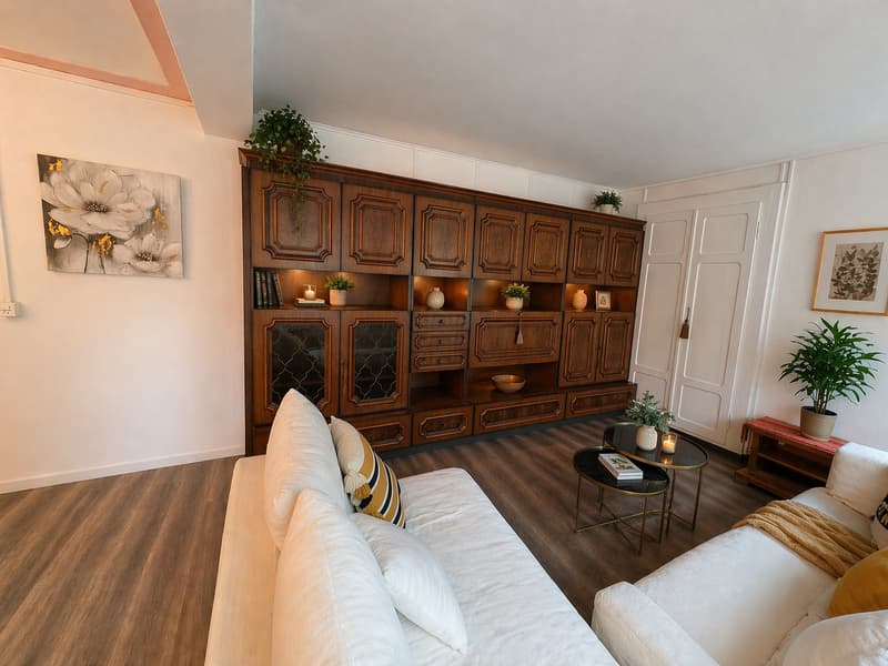 Living room with wooden floor, white walls, large wooden cabinet, two white sofas, two tables, and various potted plants.
