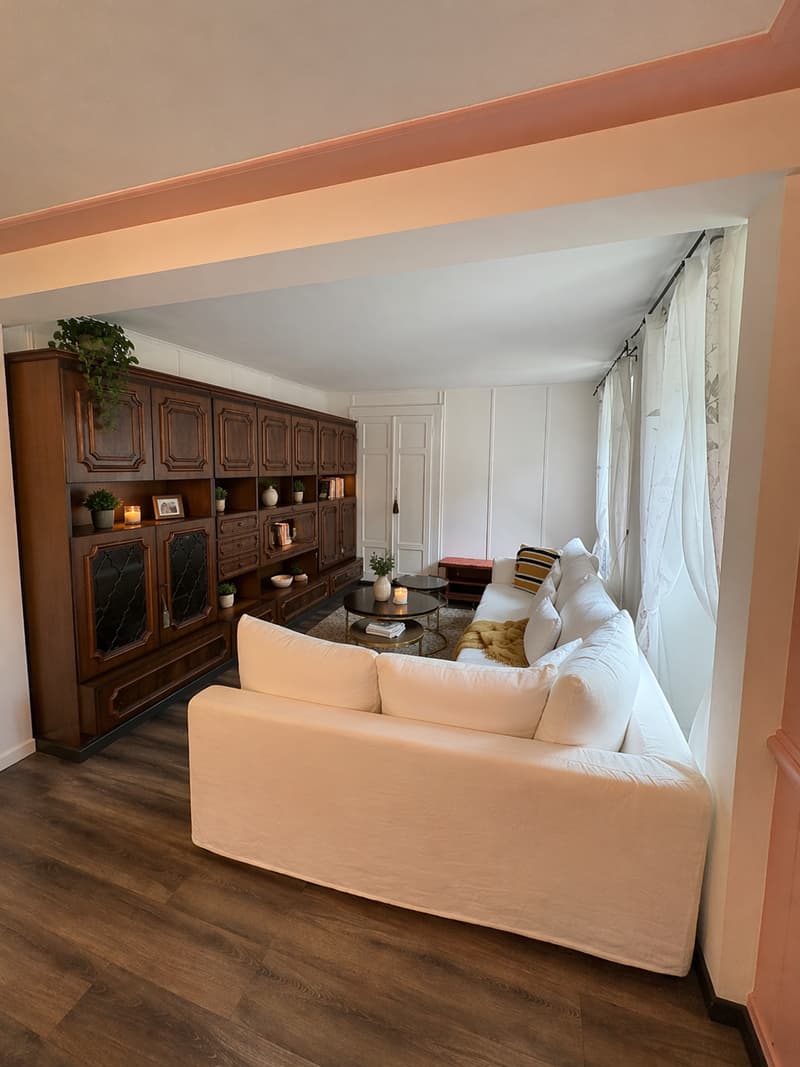 Living room with white couch, wooden floor, wooden cabinet, coffee table, side table, curtains, plants