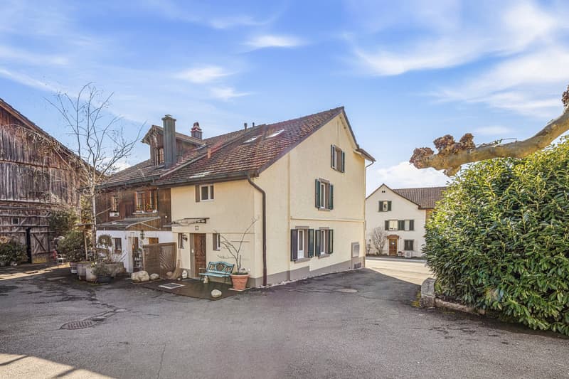 3 story house, beige exterior, brown roof, multiple windows, bench, potted plants, driveway
