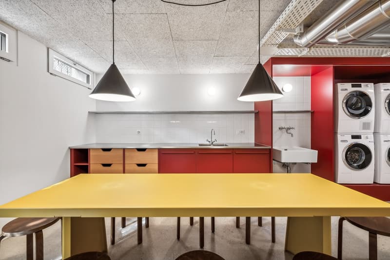 Bright and modern laundry room with a large yellow table, red cabinets, and appliances such as a washing machine and dryer.