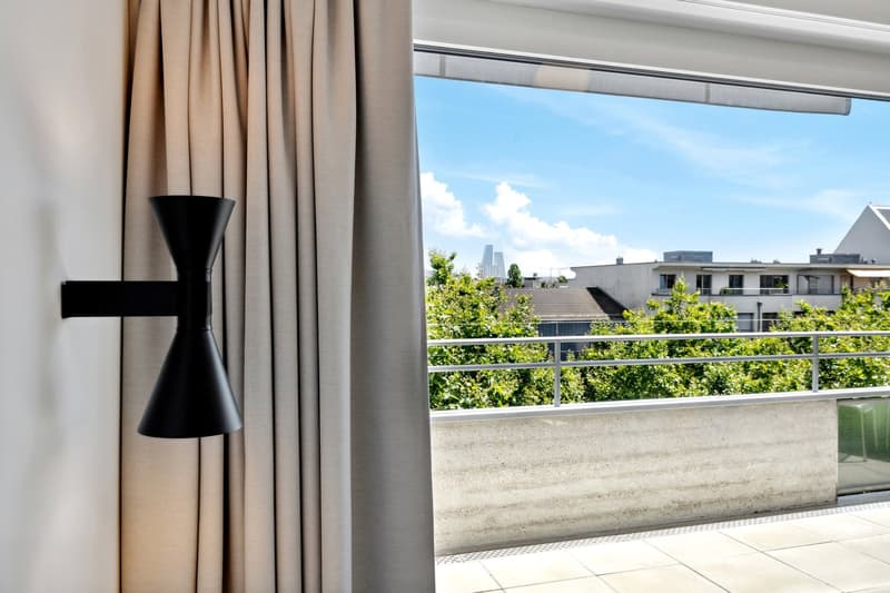 Large windows with a view of the city skyline, beige curtains, black decorative vase on the windowsill, balcony or terrace visible outside