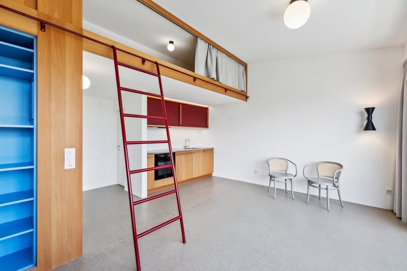 modern kitchen with red ladder, wooden cabinets, white walls, gray floor, two chairs, power outlet, and a sink with faucet