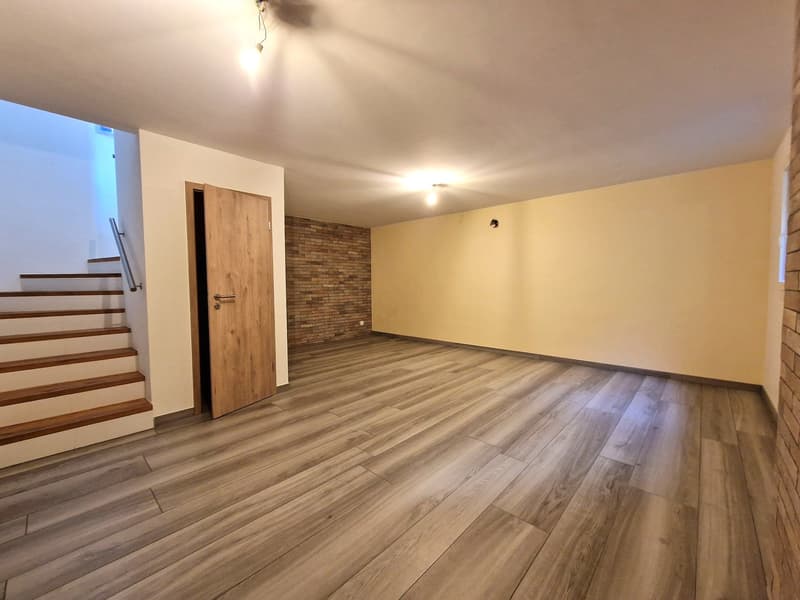 Empty room with wooden floor, white walls, brick wall, wooden door, staircase