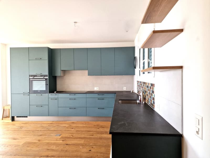 modern kitchen with blue cabinets, black countertops, wooden floor, integrated oven, sink, faucet, power outlets, tiled backsplash