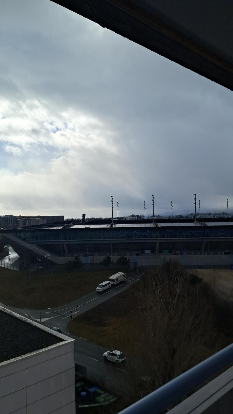 Overlooking the road with vehicles passing by, nearby there is a building with solar panels on the roof, and a bridge crossing over the road in the distance.