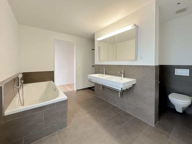 White bathtub, double sinks, separate toilet, large mirror, tiled flooring, modern design