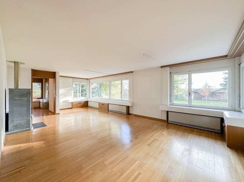 Large empty room with wooden floor, white walls, fireplace, large windows, window seats, heating systems