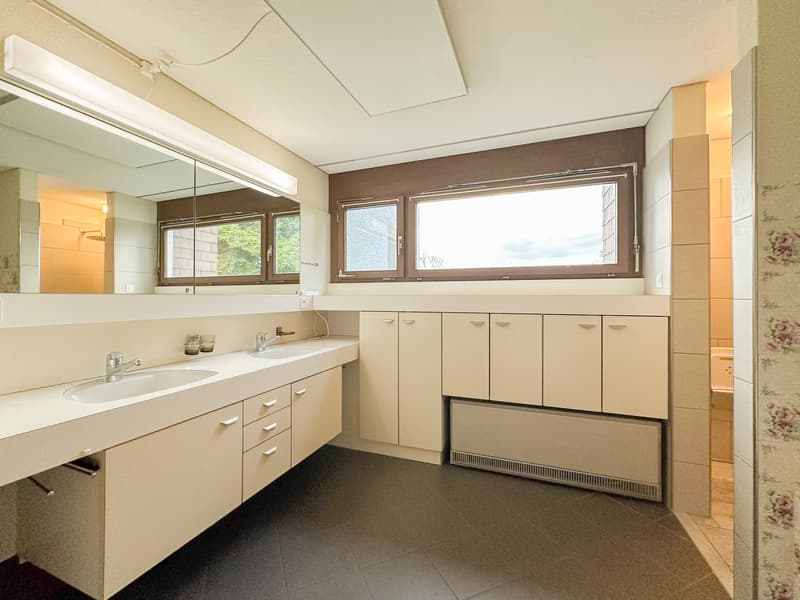 Bathroom with two sinks, cabinets, large mirror, windows, and floor heating