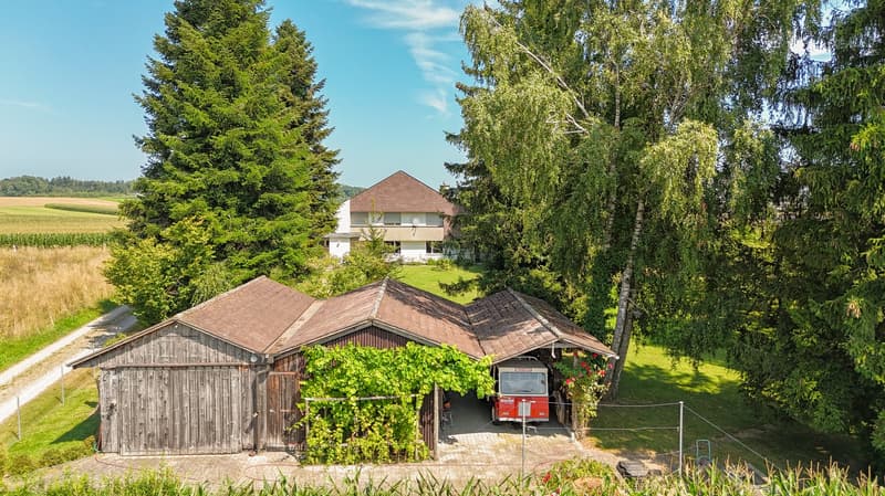 House in a rural setting, white exterior, garage with a van parked inside, surrounded by trees and grass