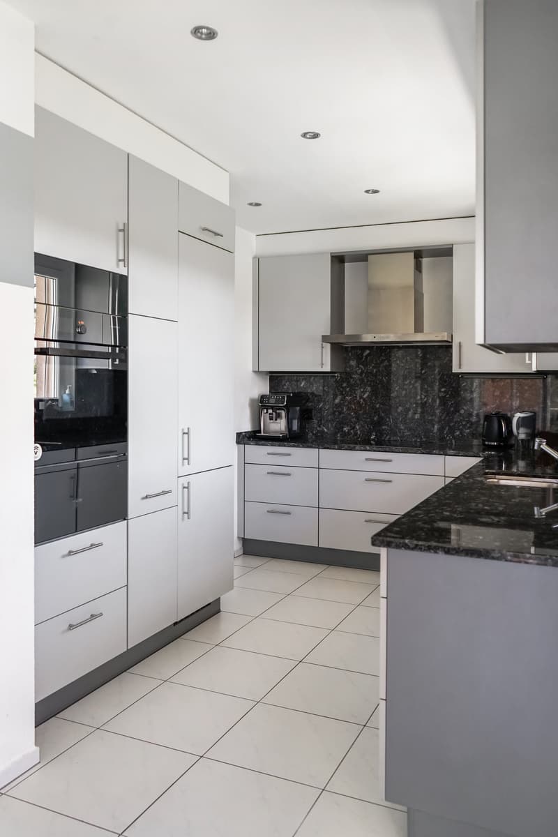 Modern kitchen with white cabinets, black granite countertops, stainless steel appliances including a refrigerator, dishwasher, and coffee maker, tiled flooring