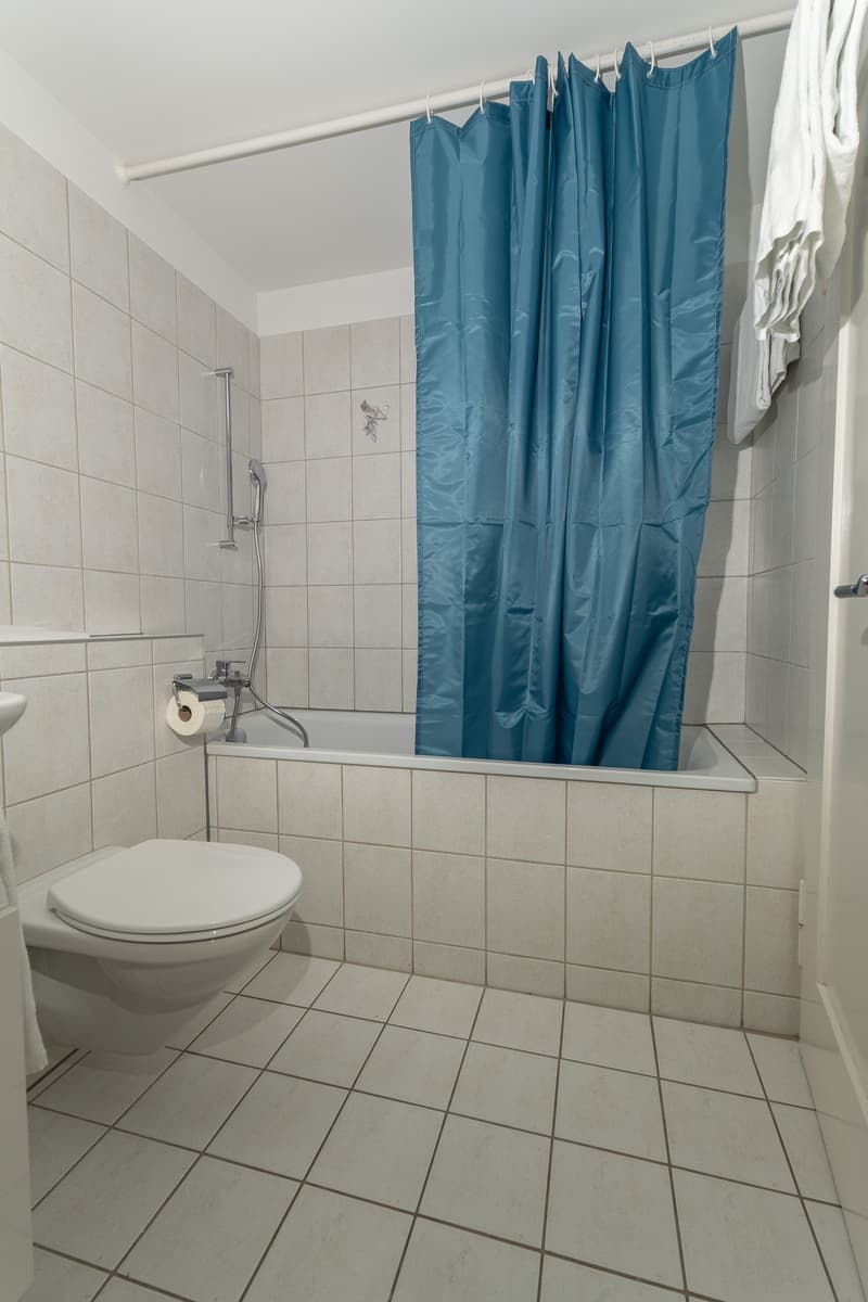 white tiles, blue shower curtain, white toilet, sink, towel bar