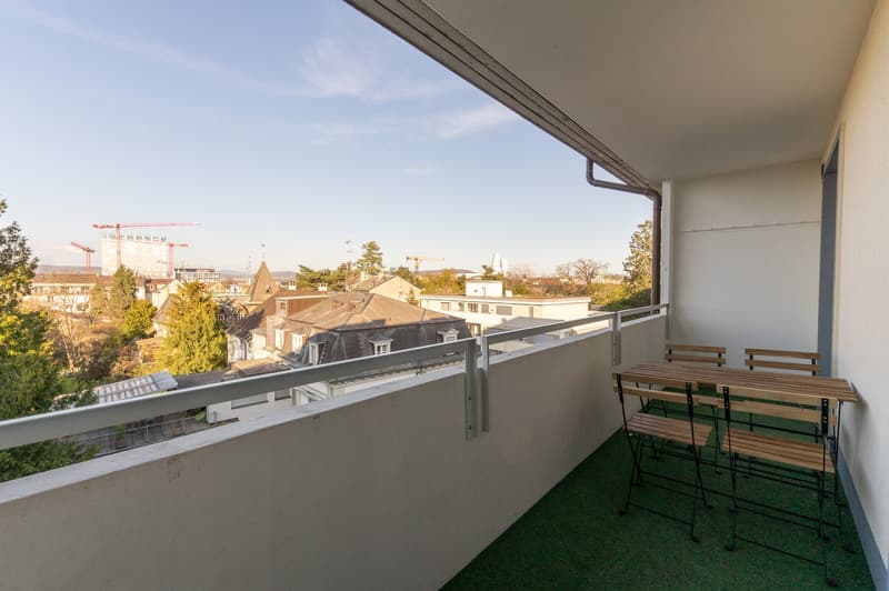 Balcony with view of the city, green grass, metal railings, table and chairs