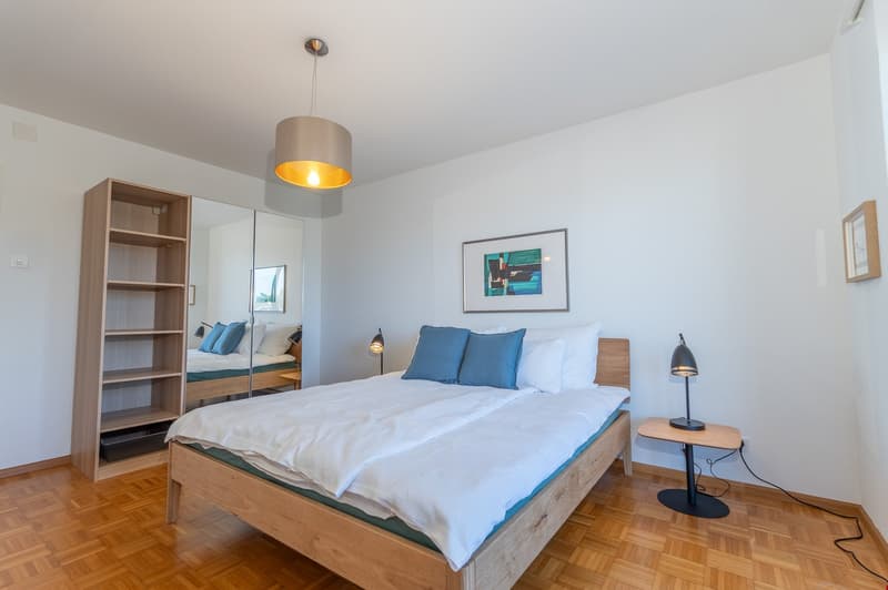 a bedroom with a wooden bed, bedside table, nightstand lamp, and a wooden shelf on the left