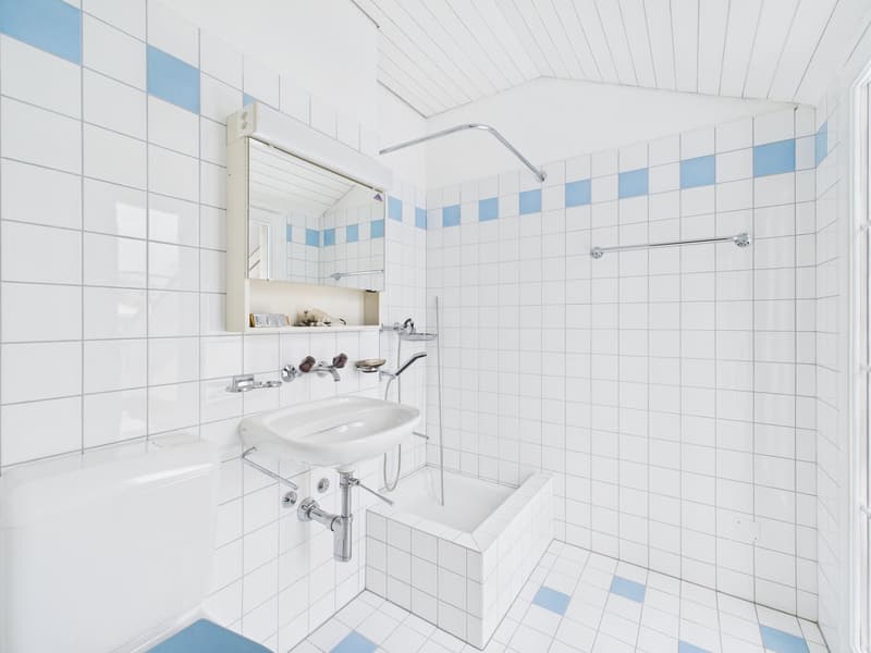 bathroom with white tiles, blue accents, toilet, sink, bathtub, and shower area