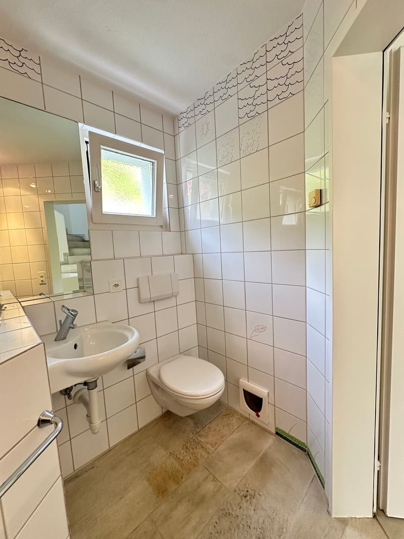 Bathroom with white tiles, white sink, white toilet, mirror, and a window