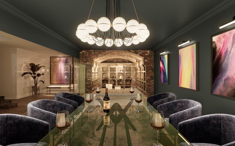 Dining room with long glass table, velvet chairs, chandelier, paintings, wine bottles and glasses