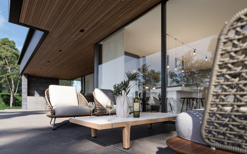 Modern outdoor seating with a wooden table, wine glasses, and a bottle, set on a tiled patio with large glass walls and hanging lights