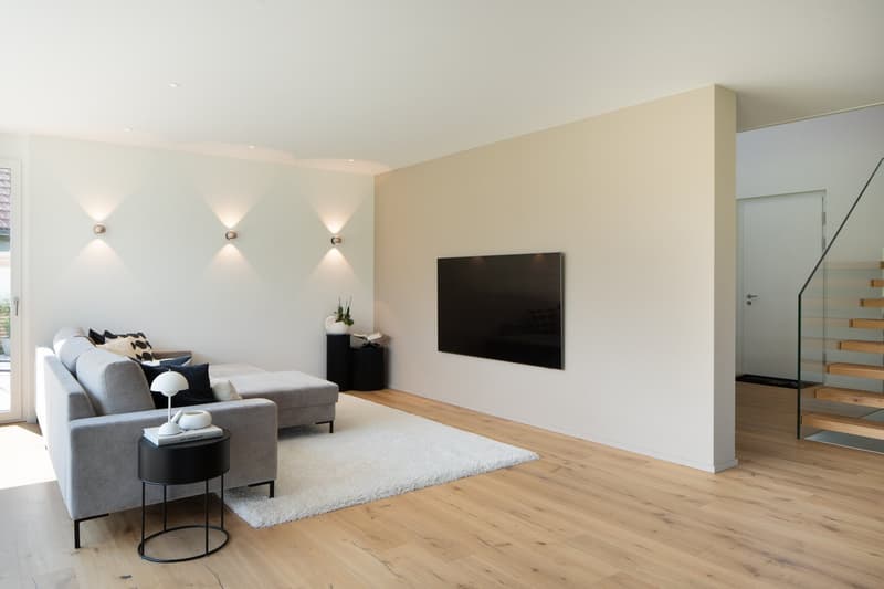 modern living room with gray sofa, white rug, black side table, mounted TV, white walls, wooden floor