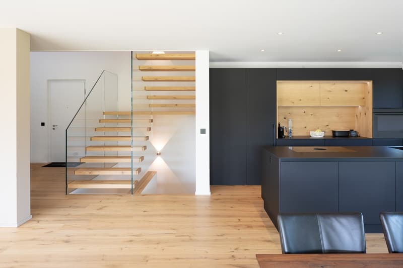 modern interior, wooden staircase, glass railing, black cabinets, wooden countertop, black leather chairs